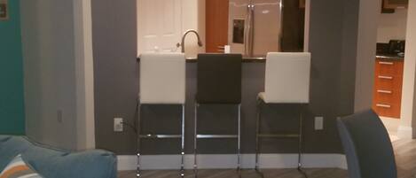 A modern kitchen with a refrigerator, sink, and bar stools.
