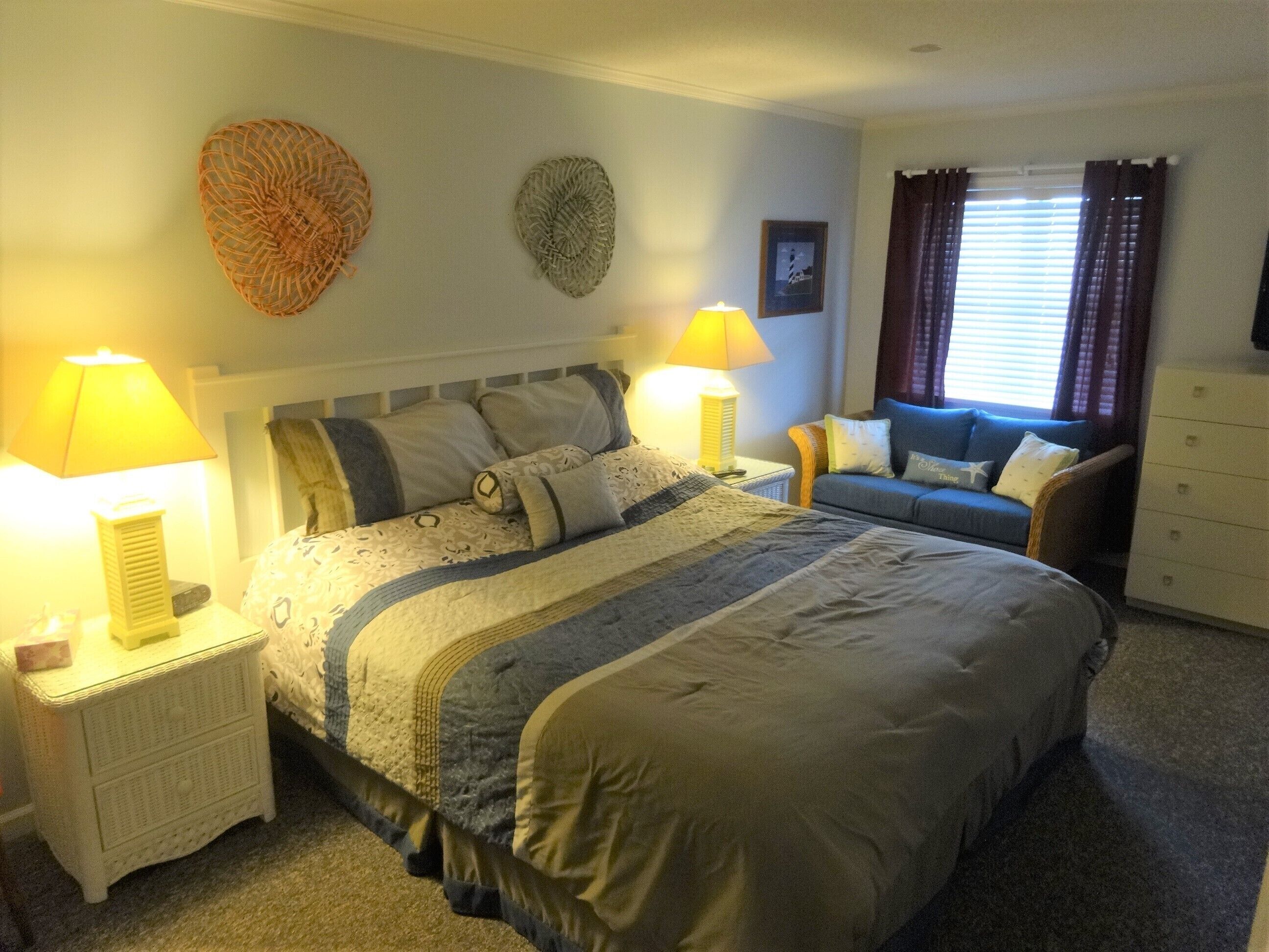 Une chambre avec un grand lit, deux tables de chevet avec des lampes, un canapé bleu et une commode.