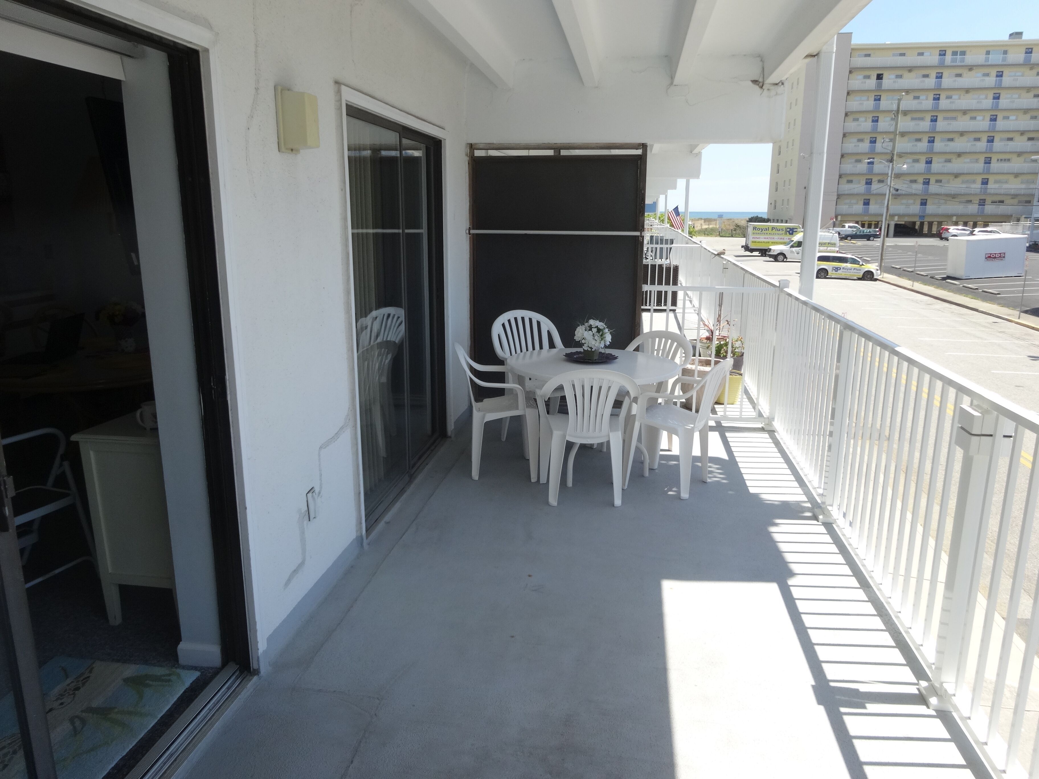 A balcony with white plastic chairs and a small table, a sliding glass door, and a white railing.