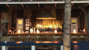 Een rustieke bar met een golfplaten dak en houten wanden, met een opvallend 'SALTLPLAGE' bord.