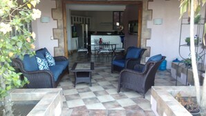 Un patio con mobiliario de mimbre, piso de baldosas y vista a la cocina.