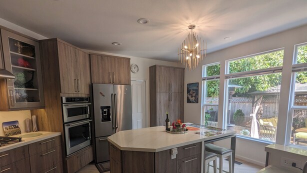 A modern kitchen with a central island, stainless steel appliances, wooden cabinets, and a large window offering a view of the backyard. - Executive Vacation House Next to Ritz-Carlton in Half Moon Bay (Half Moon Bay)