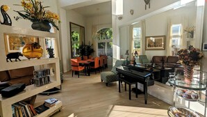 A spacious living room with a piano, a dining area, and a bookshelf filled with books. - Executive Vacation House Next to Ritz-Carlton in Half Moon Bay (Half Moon Bay)