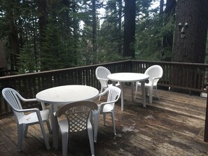 Eine Holzterrasse mit einem runden Tisch und vier Stühlen, umgeben von hohen Bäumen.