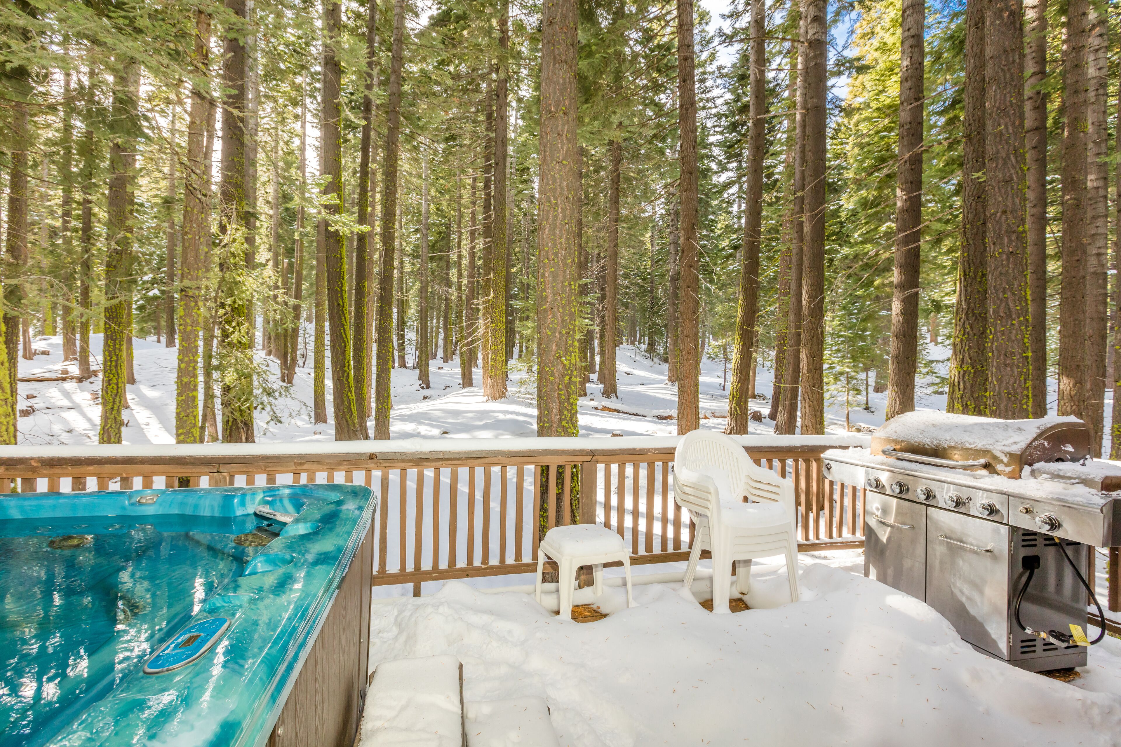 Una terraza de madera con jacuzzi, parrilla y sillas de plástico blanco.