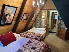 Ein gemütliches Schlafzimmer im Dachgeschoss mit zwei Betten, Holzwänden, einer Wand mit Leopardenmuster und einem gerahmten Bild eines Wolfs.