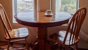 Un tavolo rotondo in legno con quattro sedie, due finestre che si affacciano sulle montagne e un pavimento con decorazione in pietra.