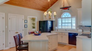 Una cocina con una isla central, armarios blancos, un refrigerador negro y una decoración con forma de velero en el techo.