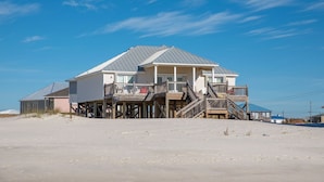 Una casa frente a la playa con balcón y una escalera que lleva a la entrada principal.