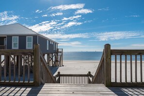 A wooden boardwalk leading to a beach with a building on the left.