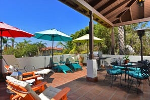 An outdoor patio with a covered seating area, umbrellas, and a grill.
