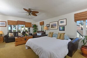 A spacious living room with a large bed, a leather sofa, and a ceiling fan.