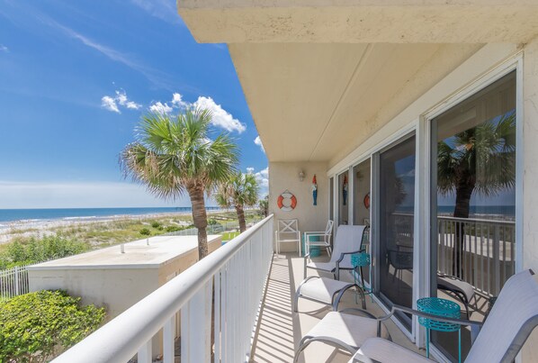 A balcony with white railings, a table, chairs, and a view of the beach and ocean. - Beachside Bliss (Jacksonville Beach)