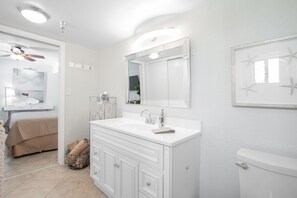 A modern bathroom with a large vanity, a ceiling fan, a toilet, and a framed artwork on the wall. - Beachside Bliss (Jacksonville Beach)