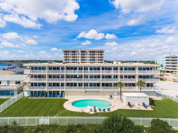 Un hotel de varios pisos con piscina, balcones y un césped vallado.