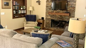 A living room with a fireplace, a mounted TV, and a bookshelf. - SPECTACULAR MOUNTAIN BLUFF CABIN WITH LAKE VIEWS-CENTRAL AC! (Pinetop-Lakeside)