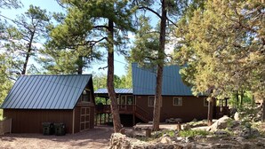 A rustic cabin with a metal roof, surrounded by trees and a stone wall. - SPECTACULAR MOUNTAIN BLUFF CABIN WITH LAKE VIEWS-CENTRAL AC! (Pinetop-Lakeside)
