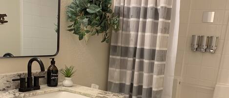Un bany amb un lavabo de marbre, armaris de fusta, un vàter, una cortina de bany i una planta en test.
