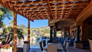 An outdoor patio with wicker furniture, a pool, and a pergola with patterned beams. - THE RETREAT, an Executive Custom Home in Estrella Mtns! (Goodyear)