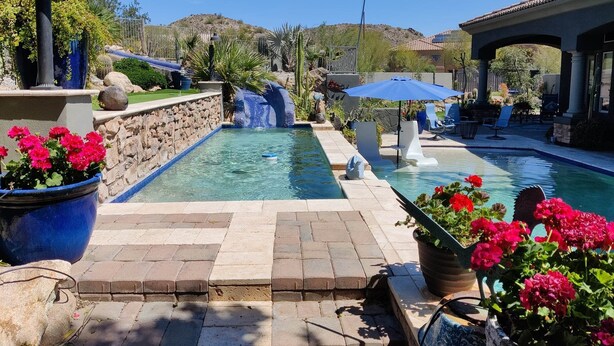 A swimming pool with a waterfall feature, surrounded by potted plants and outdoor seating. - THE RETREAT, an Executive Custom Home in Estrella Mtns! (Goodyear)