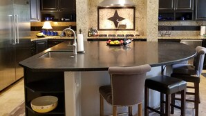 A modern kitchen with a central island, dark cabinetry, granite countertops, and a built-in stove. - THE RETREAT, an Executive Custom Home in Estrella Mtns! (Goodyear)