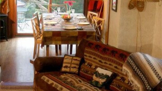 A cozy living room with a wooden sofa, a dining table set for two, and a view of the outdoors through a large window. - Fly Fishing River Chalet, Fly Shop, Guides, Schools, & Kayaks! (River Falls)