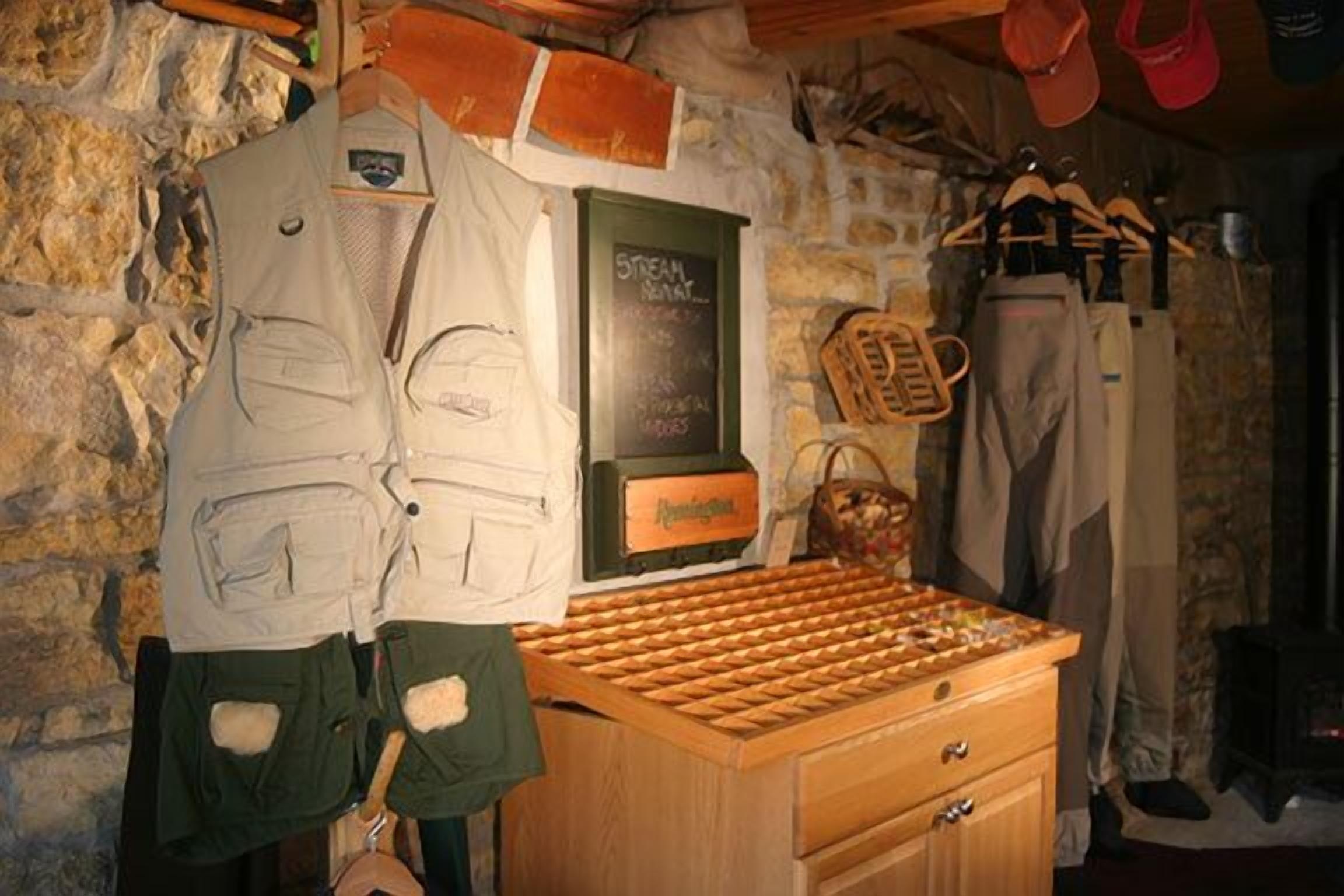 Una habitación rústica con pared de piedra, un cofre de madera y un perchero con equipo de senderismo.