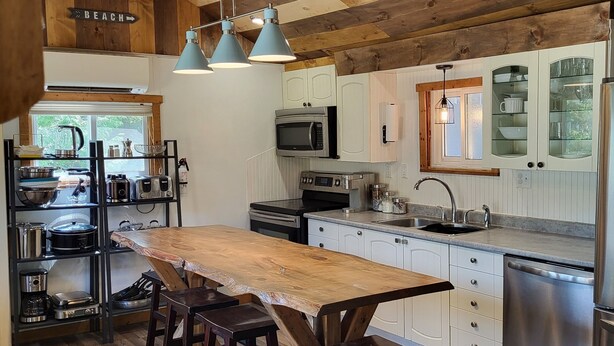 A modern kitchen with a wooden ceiling, a central island with stools, and stainless steel appliances. - Sandy Trail Lodge 3 Bedroom Cottage Backs on to Sauble Beach  (Sauble Beach)