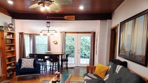 A living room with a sofa, a coffee table, a bookshelf, a dining table, and a chandelier. - Sandy Trail Lodge 3 Bedroom Cottage Backs on to Sauble Beach  (Sauble Beach)