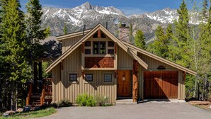 Une cabane en bois avec une cheminée en pierre, un garage et une allée menant à un escalier en bois.