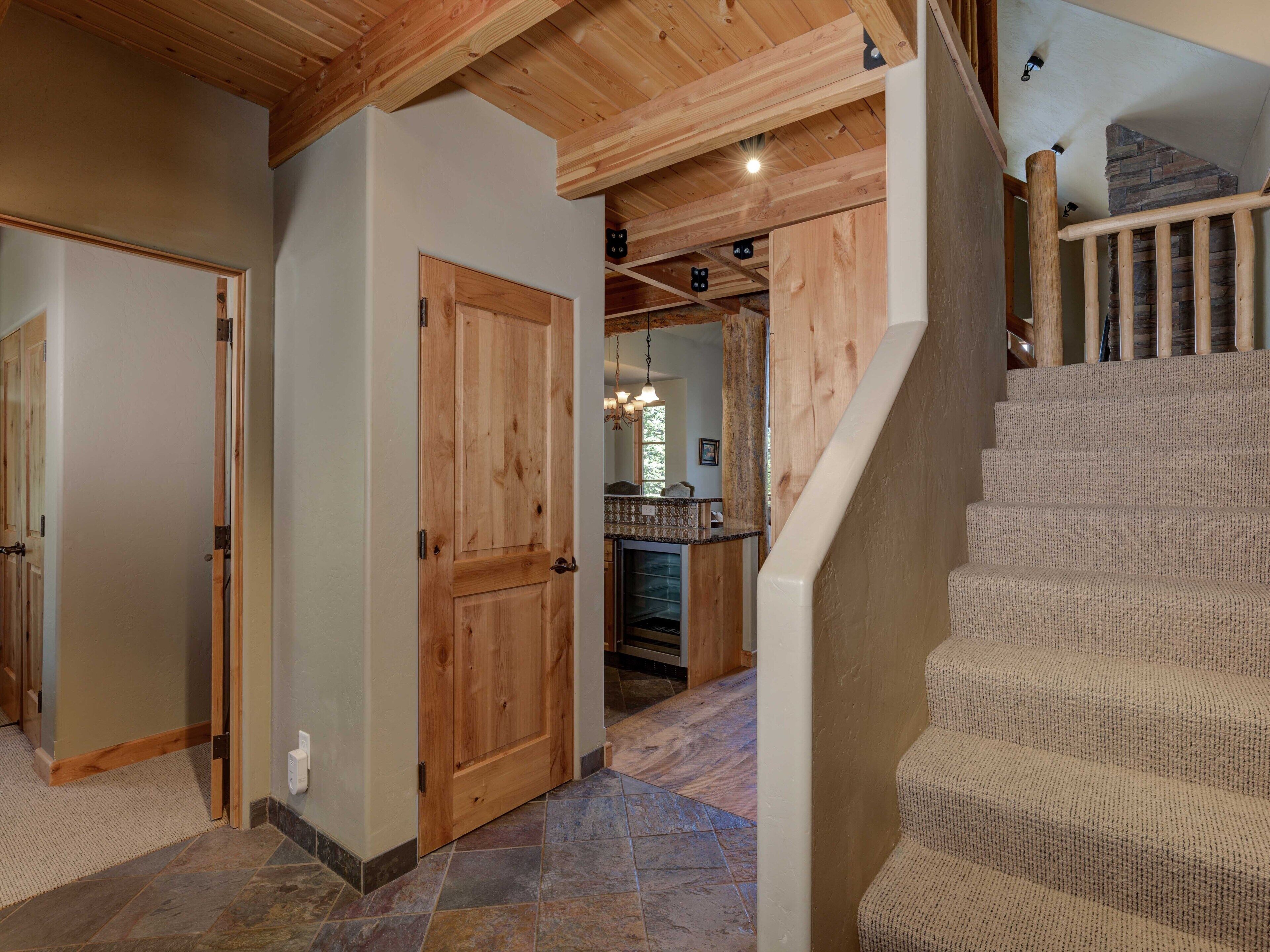 A wooden staircase with a textured carpet, a stone-tiled floor, and a wooden door.