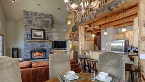 Un salon chaleureux avec une cheminée en pierre, un canapé en cuir et un coin repas avec une table en bois mise pour quatre personnes.