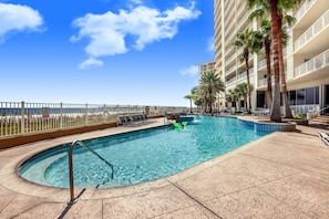 A hotel pool with a clear view of the ocean, a palm tree-lined deck, and a fenced area with lounge chairs.