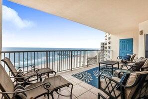 A balcony with a view of the ocean, furnished with chairs and a table, and a blue door. - Admiral Quarters 2BR 2.5BA, SUPER NICE, 1521sf, Aug availability (Orange Beach)