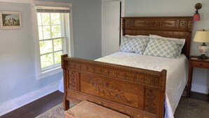 A bedroom with a wooden bed, a nightstand with a lamp, a window with blinds, and a framed picture on the wall. - Waterfront! Charming 4BR Cottage on the Niantic River!  (Waterford)