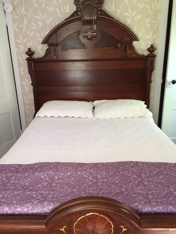 Uma cama de madeira com cabeceira, duas almofadas e um edredom roxo estampado.