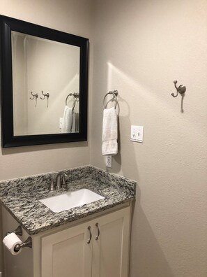 A bathroom with a granite countertop sink, a mirror, towel hooks, and a toilet paper holder. - Beautiful Pool - 2 BR/2 BA - 1 Mile to Beach (Port Aransas)