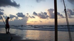 Escena de playa con una persona cerca del agua, cuerdas y un atardecer al fondo.