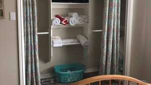 Un dormitorio con cama, cabecera de madera, armario con cortinas estampadas y cesta de ropa en color aguamarina.