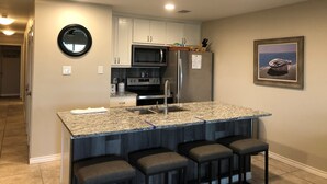 Una cocina moderna con encimeras de granito, electrodomésticos de acero inoxidable y una zona de bar con taburetes.