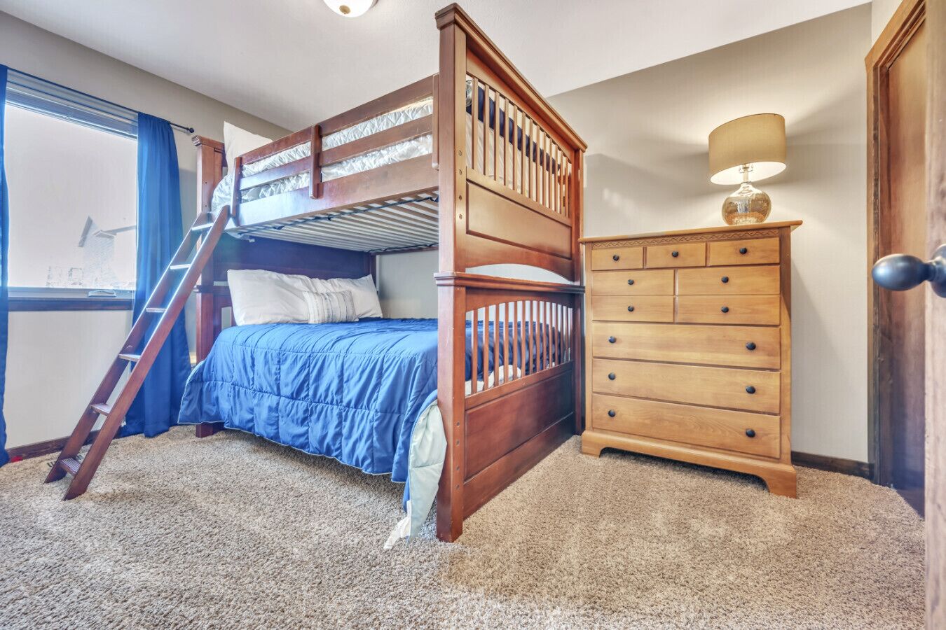 A bedroom with a bunk bed, a dresser, a lamp, and a window with curtains.