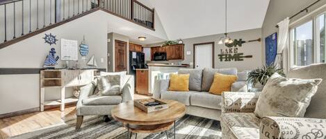 A spacious living area with a high ceiling, a staircase, a kitchen, and a dining area.