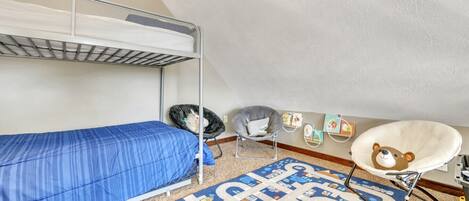 A dormitory room with bunk beds, a desk, a chair, a rug, and wall decorations.