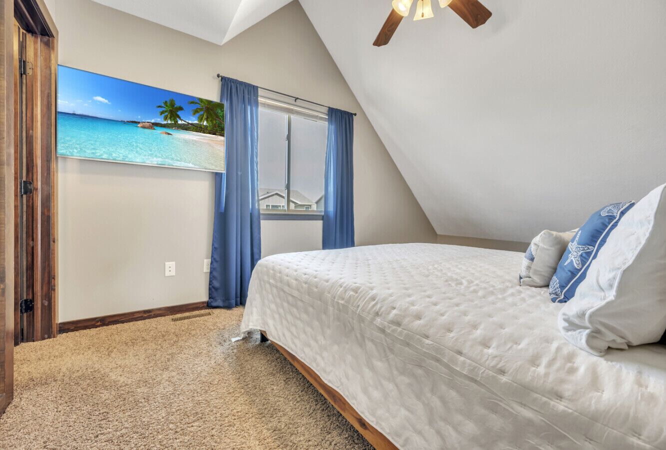 A bedroom with a large window, a bed with white bedding, and a view of a beach.