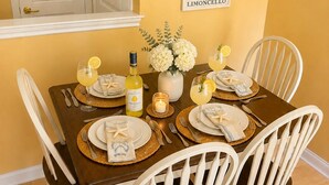Mesa para cuatro personas con sillas blancas, un cuadro en la pared y una botella de Limoncello.