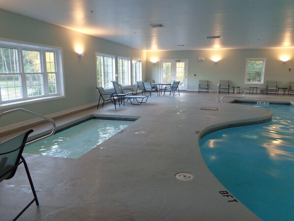 En indendørs swimmingpool med flere baner, liggestole og borde.