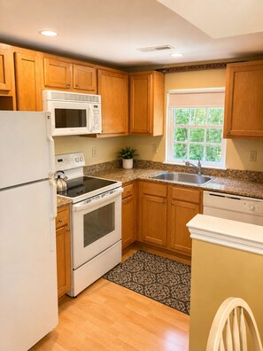 A kitchen with wooden cabinets, a microwave, stove, sink, and a window with a view. - Goose Rocks Beach!!  Sunny bright condo. (Kennebunkport)