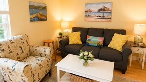 Un salon comprenant un canapé, un fauteuil et une table basse, ainsi qu’une petite table d’appoint et deux lampes fixées au mur.