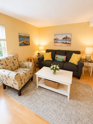 A living room with a sofa, armchair, and coffee table, a small side table, and two wall-mounted lamps. - Goose Rocks Beach!!  Sunny bright condo. (Kennebunkport)