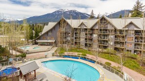 A hotel with a pool, multiple balconies, and a mountainous backdrop. - SKI IN/OUT, close to gondola and village - 1 bd, Hot Tubs/pool (Whistler)